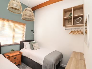 A bedroom with two single beds bedside table wooden shelving and hanging rail with hangers at Tolcarne in Porthtowan
