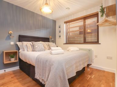 A bedroom with a double bed with pillows and folded towels a wooden floor and window blinds at Tolcarne Porthtowan