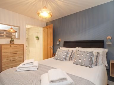 A bedroom with a bed with patterned pillows towels on the bed a wooden dresser and an open door to a bathroom at Tolcarne in Porthtowan