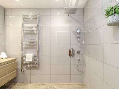 A bathroom with a walk-in shower a towel rack a wooden cabinet and a hanging plant at Tolcarne in Porthtowan