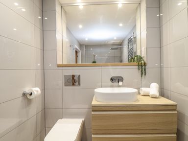 A bathroom with a wooden vanity, round sink, large mirror, toilet, and towel rolls at Tolcarne in Porthtowan