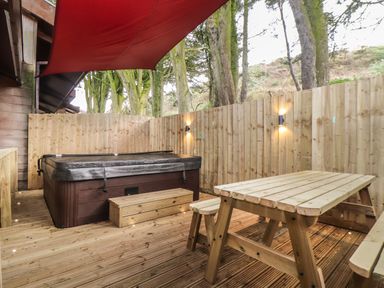 An outdoor wooden deck with a hot tub and wooden picnic table under a red canopy at Tolcarne in Porthtowan