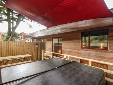 An outdoor patio area with a hot tub under a red canopy next to wooden fencing and a wooden picnic table at Tolcarne in Porthtowan