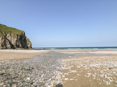 A sandy beach with scattered white stones and a rocky cliff beside the sea at Tolcarne in Porthtowan
