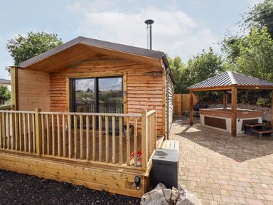 An outdoor patio with a wooden cabin and a covered hot tub at Celyn in Cyffylliog