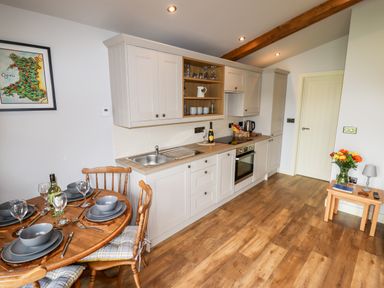 A kitchen with white cabinets wooden floor a dining table with place settings and a small table with flowers at Celyn in Cyffylliog