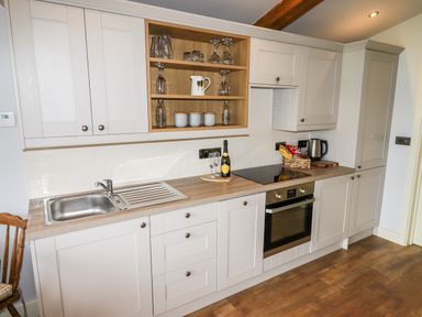 A kitchen with white cabinets wooden countertop sink stove oven and open shelves with glasses at Celyn in Cyffylliog