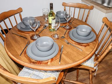 A wooden round dining table with four place settings with gray plates bowls and wine glasses and a bottle of white wine at Celyn in Cyffylliog
