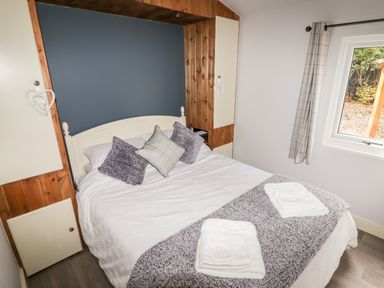 A bedroom with a double bed white bedding pillows and folded towels near a window at Celyn in Cyffylliog