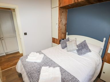A bedroom with a double bed made with white and gray bedding two towels on the bed wooden paneling around the headboard and a doorway showing cupboards at Celyn in Cyffylliog