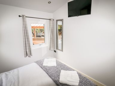 A bedroom with a bed with folded towels a window with curtains a wall mirror and a mounted television at Celyn in Cyffylliog