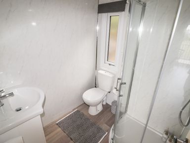 A bathroom with a sink, toilet, shower enclosure, a window, and a small rug on the floor at Celyn in Cyffylliog