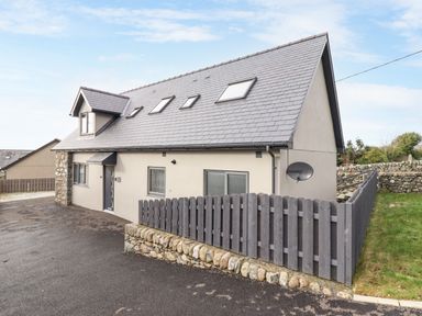A modern two-story house with slate roof windows and a wooden fence surrounding part of the property at Bryn Hafod in Dyffryn Ardudwy