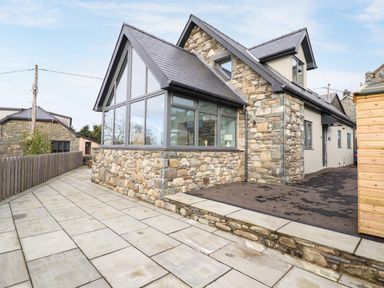 A stone and glass house with a paved pathway and a wooden fence at Bryn Hafod in Dyffryn Ardudwy