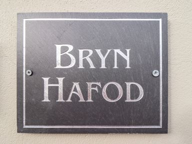 A black rectangular plaque with the text Bryn Hafod mounted on a beige wall at Bryn Hafod in Dyffryn Ardudwy
