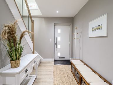 A hallway with a white door a coat rack a bench with cushions and baskets a white table with a plant and a stairway at Bryn Hafod in Dyffryn Ardudwy