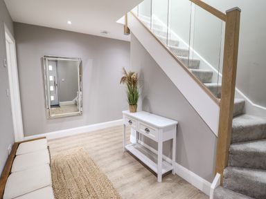 A hallway with a bench a rug a mirror a white table with a plant and carpeted stairs at Bryn Hafod in Dyffryn Ardudwy