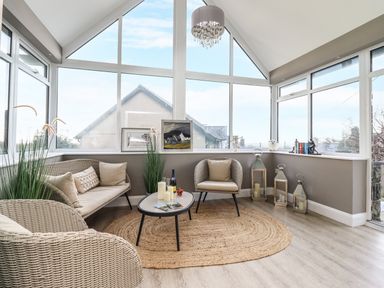 A seating area with wicker furniture a small table and large windows at Bryn Hafod in Dyffryn Ardudwy