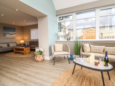 A sitting area with armchairs a wicker sofa coffee table and large windows at Bryn Hafod in Dyffryn Ardudwy