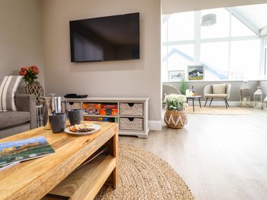 A living room with a wooden coffee table holding cups and snacks a TV mounted on the wall and wicker basket with flowers at Bryn Hafod in Dyffryn Ardudwy