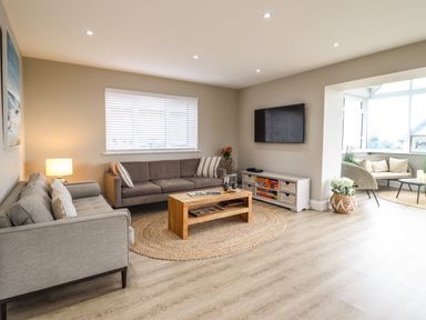 A living room with sofas a wooden coffee table a wall-mounted TV and a seating area with chairs at Bryn Hafod in Dyffryn Ardudwy