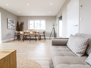 A dining area with a wooden table and chairs next to a window and a seating area with a sofa and cushions at Bryn Hafod in Dyffryn Ardudwy