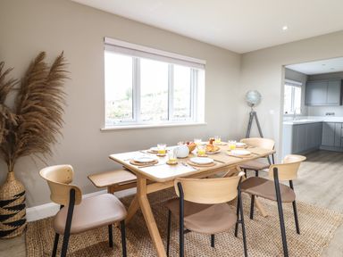 A dining area with a wooden table set for breakfast and six chairs near a window at Bryn Hafod in Dyffryn Ardudwy