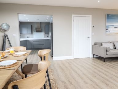 A dining area with wooden table and chairs next to a kitchen with grey cabinets and a living room with a sofa at Bryn Hafod in Dyffryn Ardudwy