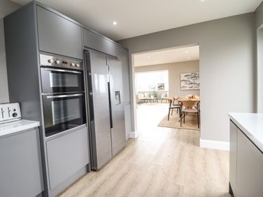 A kitchen with gray cabinets a double oven a stainless steel refrigerator and a dining area with table and chairs at Bryn Hafod in Dyffryn Ardudwy