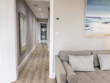 A hallway with wooden flooring and a mirror on the wall adjacent to a living room with a grey sofa and pillows at Bryn Hafod in Dyffryn Ardudwy