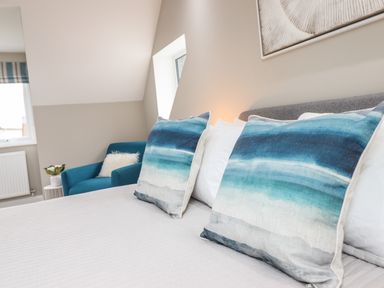 A bedroom with a bed featuring blue gradient pillows and a blue armchair with a white cushion at Bryn Hafod in Dyffryn Ardudwy