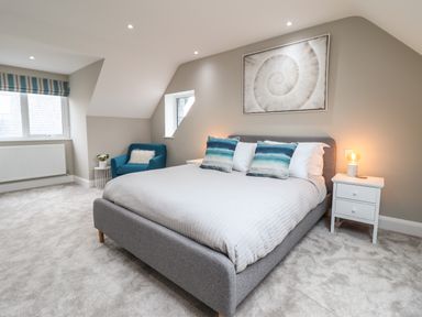 A bedroom with a bed with blue and white pillows a blue armchair bedside tables with lamps and a picture on the wall at Bryn Hafod in Dyffryn Ardudwy