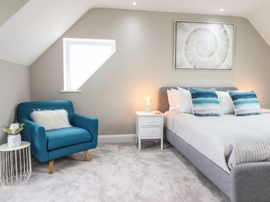 A bedroom with a blue armchair a bedside table with a lamp and a bed with blue pillows at Bryn Hafod in Dyffryn Ardudwy