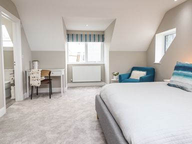 A bedroom with a bed a blue armchair a small white desk and an open door to a bathroom at Bryn Hafod in Dyffryn Ardudwy