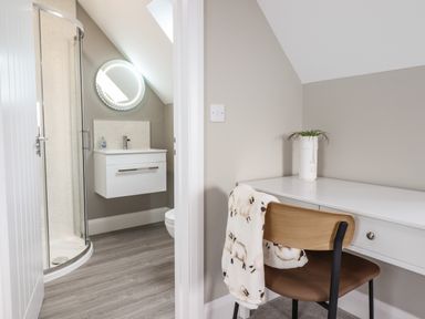 A small bathroom with a shower and vanity next to a white desk with a chair and a plant at Bryn Hafod in Dyffryn Ardudwy