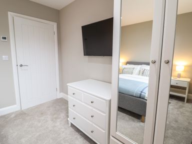 A bedroom with a white chest of drawers a wall-mounted tv and a mirrored wardrobe at Bryn Hafod in Dyffryn Ardudwy