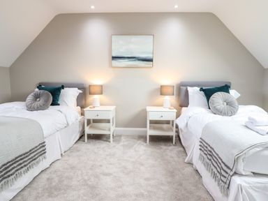 A bedroom with two single beds side by side with white bedding grey and teal cushions two white bedside tables each with a lamp a painting above Bryn Hafod in Dyffryn Ardudwy
