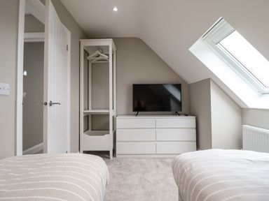A bedroom with two beds a white dresser with a TV on top a tall white wardrobe and a skylight window at Bryn Hafod in Dyffryn Ardudwy