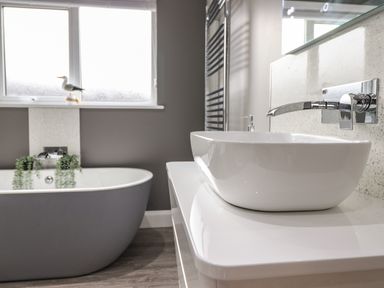A bathroom with a gray freestanding bathtub a white vessel sink and a window with a bird decoration at Bryn Hafod in Dyffryn Ardudwy