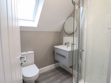 A bathroom with a toilet a sink with a cabinet a round mirror and a glass shower enclosure at Bryn Hafod in Dyffryn Ardudwy