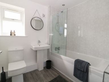 A bathroom with a toilet sink round mirror bathtub with shower and towel at Chalet 1 Sherburn