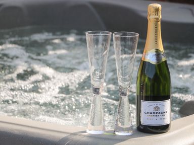 A bottle of champagne and two empty glasses on the edge of a hot tub at Chalet 1 in Sherburn