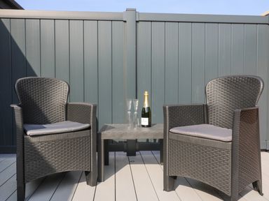 Two black wicker chairs with cushions and a small black table with a bottle and two glasses on a deck at Chalet 1 Sherburn