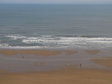 A sandy beach with small waves and two people walking near the water at Chalet 1 in Sherburn