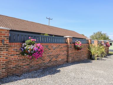 A brick wall with hanging flower baskets and a gravel path at Chalet 1 in Sherburn