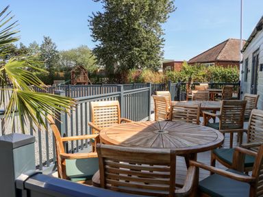 An outdoor seating area with wooden tables and chairs near a playground at Chalet 1 in Sherburn
