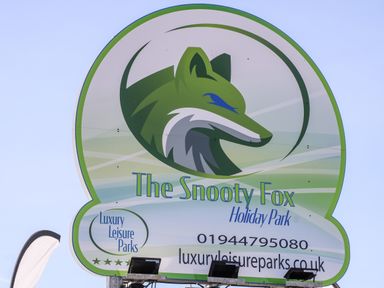 A sign with a green fox logo and text for The Snooty Fox Holiday Park with contact information