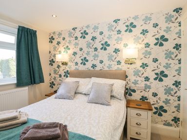 A bedroom with a double bed two bedside tables and floral wallpaper at Caradoc Tutshill near Chepstow
