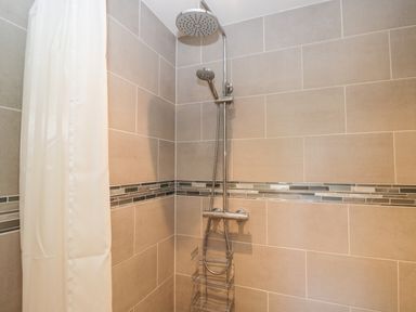 A shower area with beige tiles a rainfall showerhead and a white shower curtain at Caradoc Tutshill near Chepstow