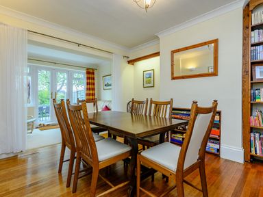 A dining room with a wooden table and chairs next to a bookshelf and a seating area at Caradoc in Tutshill near Chepstow